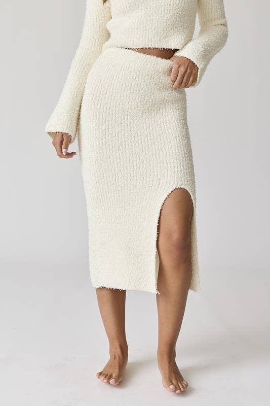 Woman wearing a white round neck long sleeve crop soft knit top and midi skirt set with a side slit.
