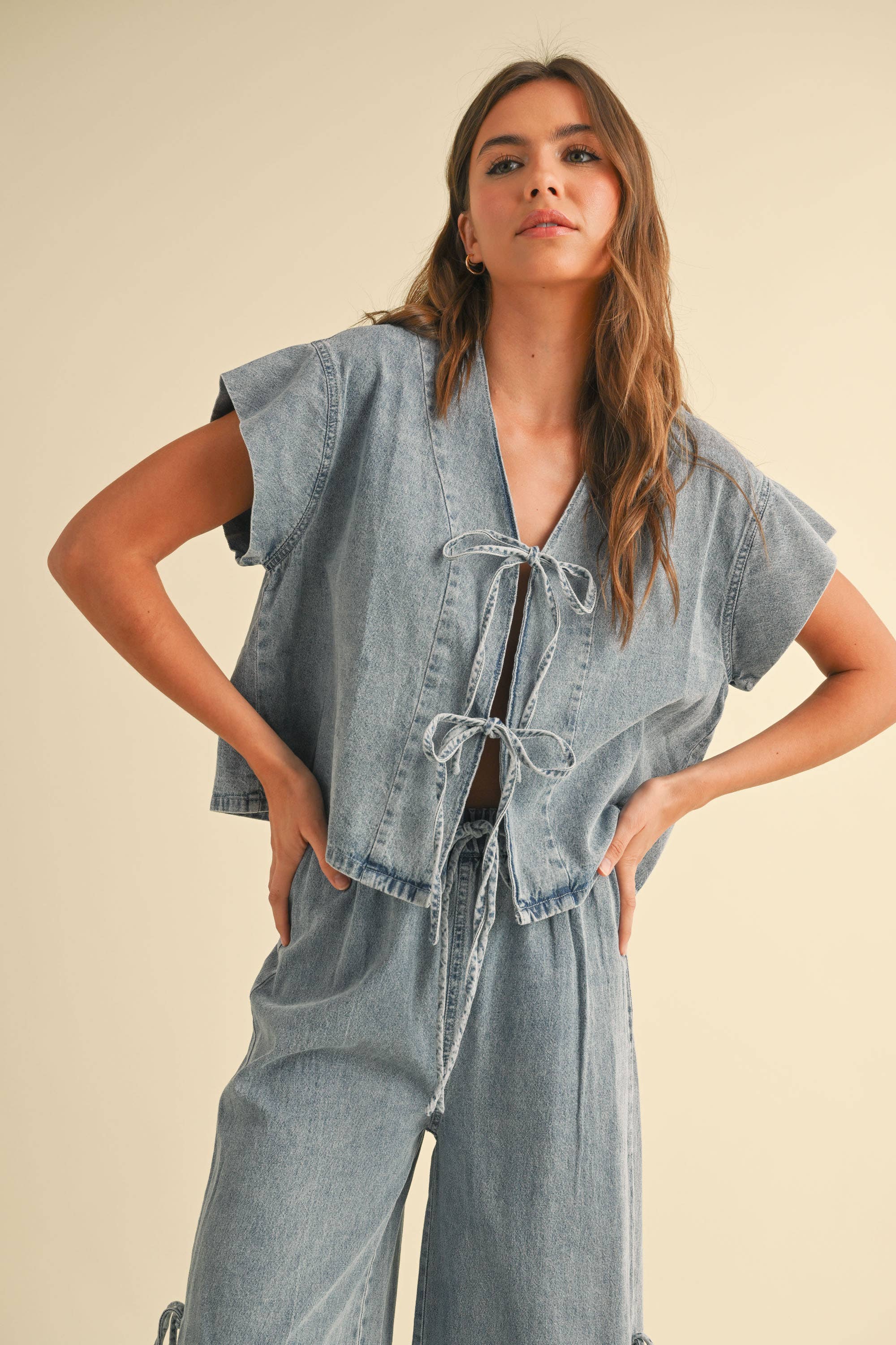 Woman wearing a light-wash denim two-piece set with tie-front top and wide-leg pants featuring side tie accents.