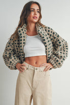Woman wearing a beige and green checkered fleece jacket with a zip closure, paired with a white crop top and beige corduroy pants.