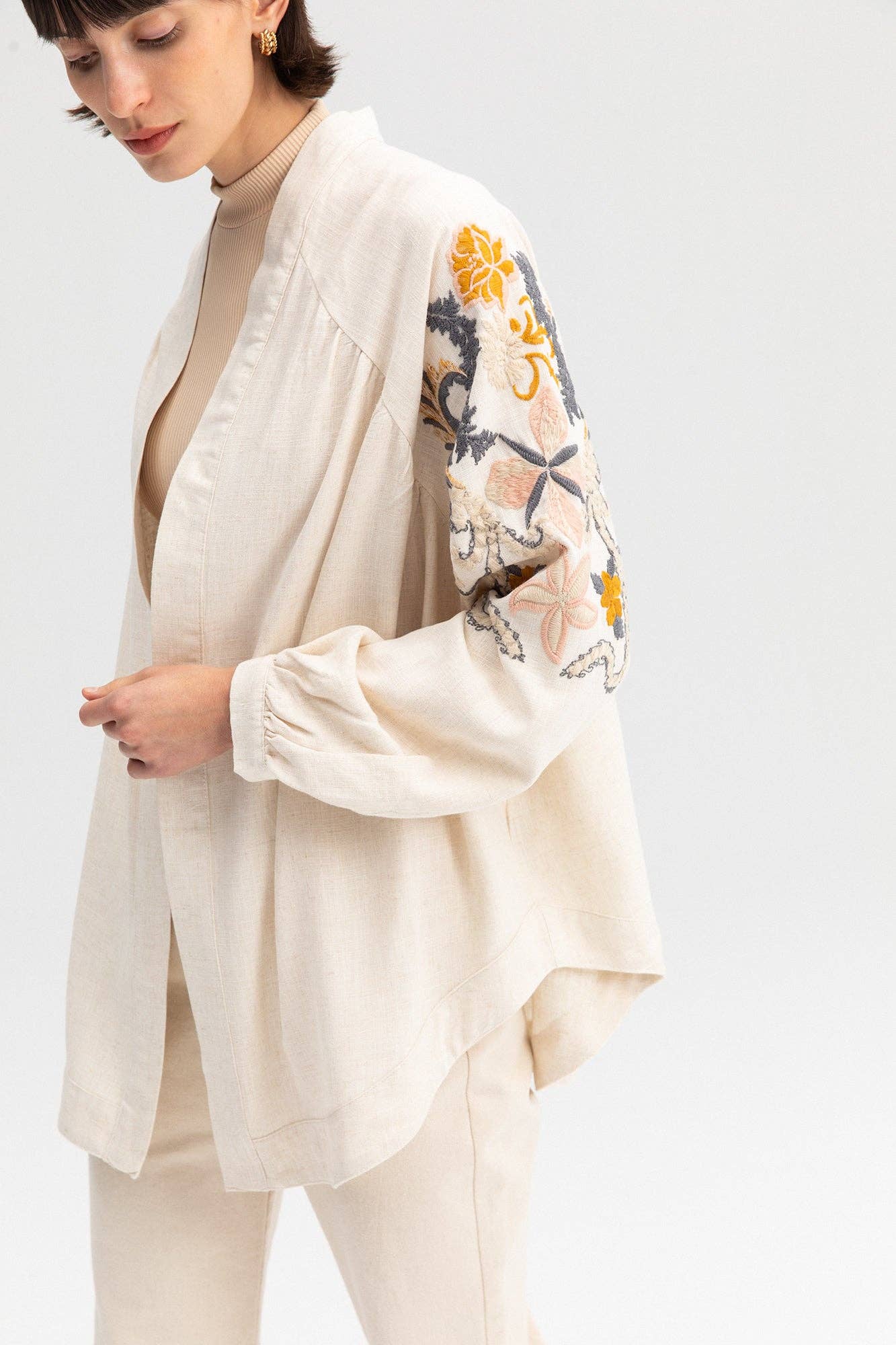 Back view of a cream-colored kimono jacket with colorful floral embroidery, worn with matching light trousers.
