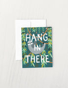 Greeting card with a sloth hanging from a tree branch and the phrase “Hang in There” surrounded by green leaves.