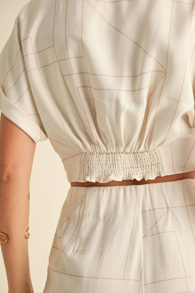 Woman wearing a cream two-piece set with geometric line print, knotted crop top, and wide-leg pants.