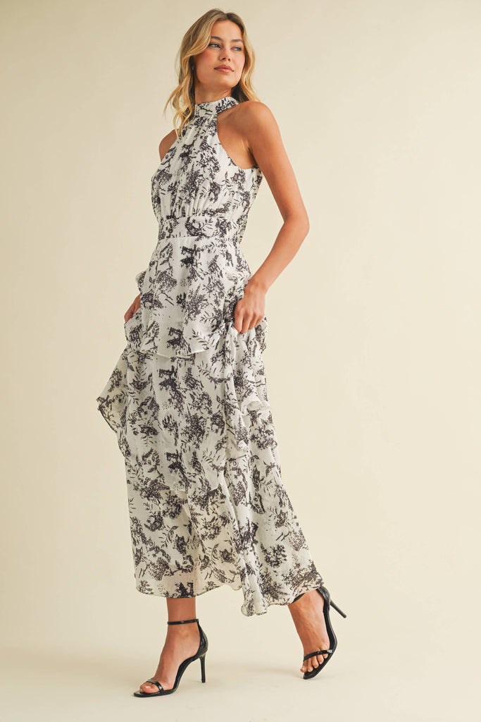 Woman wearing a halter neck tiered maxi dress with black floral print and ruffle layers