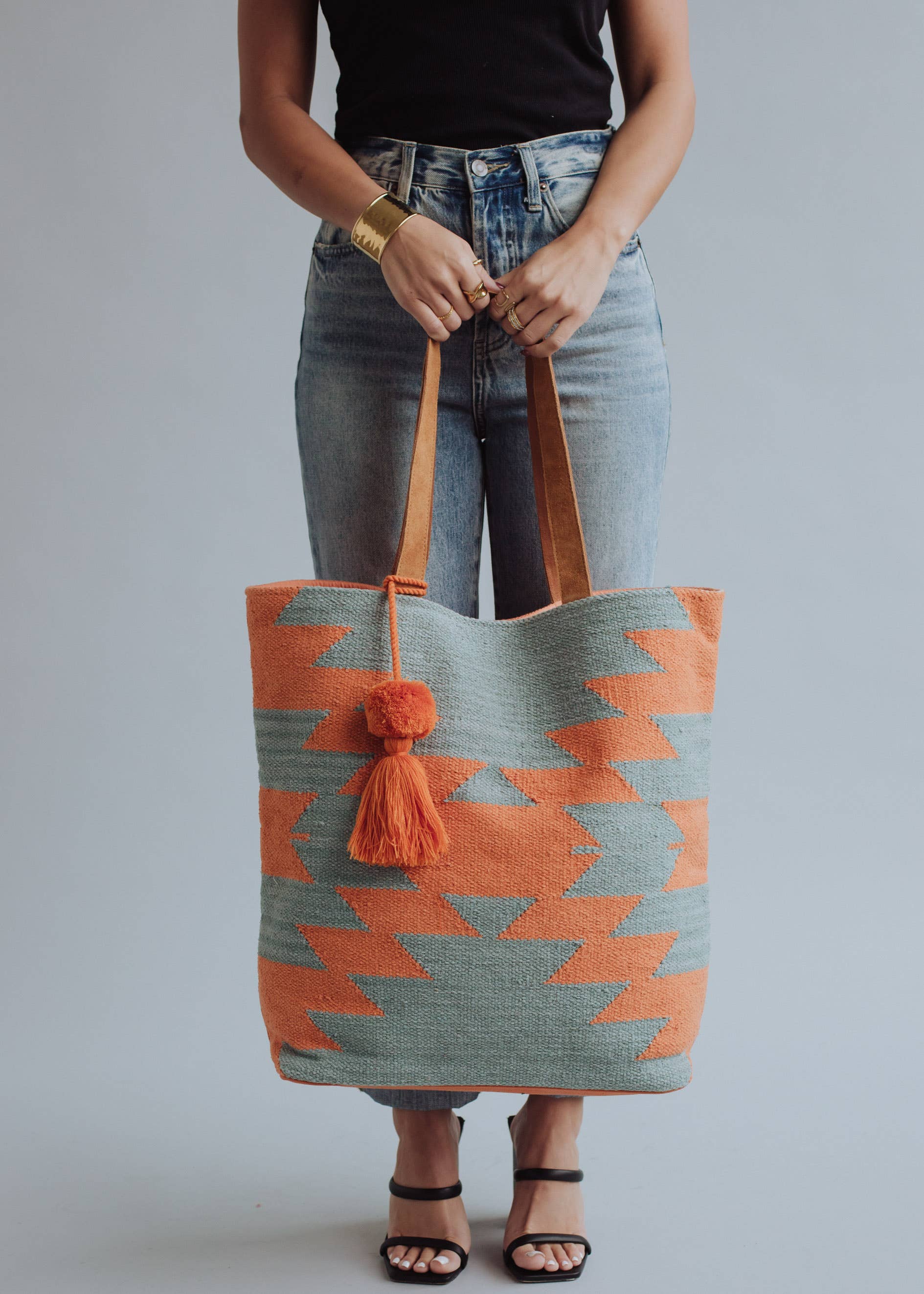 Tote bag with orange and sage green zigzag design and tassel, styled with denim jeans