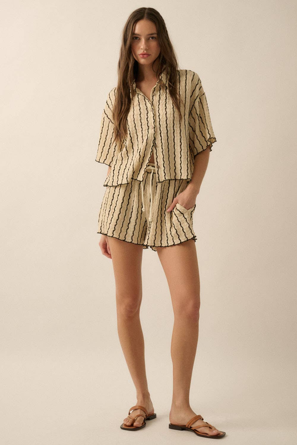 Woman wearing a beige striped two-piece lounge set with button-up shirt and matching drawstring shorts.