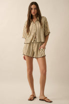 Woman wearing a beige striped two-piece lounge set with button-up shirt and matching drawstring shorts.