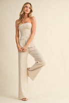 Woman wearing a strapless beige jumpsuit on a plain background