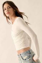 Woman wearing white long-sleeve draped top with asymmetrical ruching.