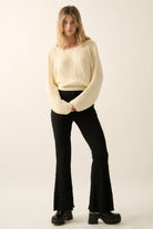 Woman wearing a cream lightweight knit sweater with wide sleeves and a cropped fit.