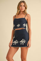 Woman wearing the Calista Set—navy two-piece with scalloped embroidered crop top and matching mini skirt.