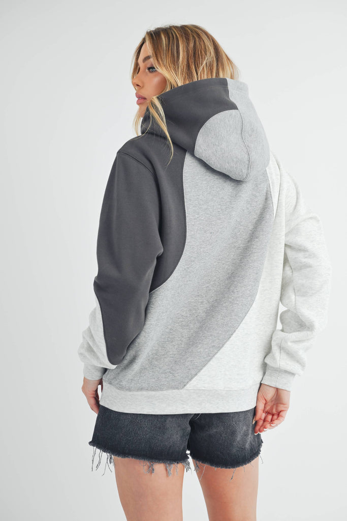 Woman wearing an oversized colorblock hoodie in grey, black, and ivory with a relaxed fit and kangaroo pocket.