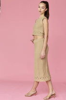 Woman wearing a beige sleeveless crochet top and midi skirt set.