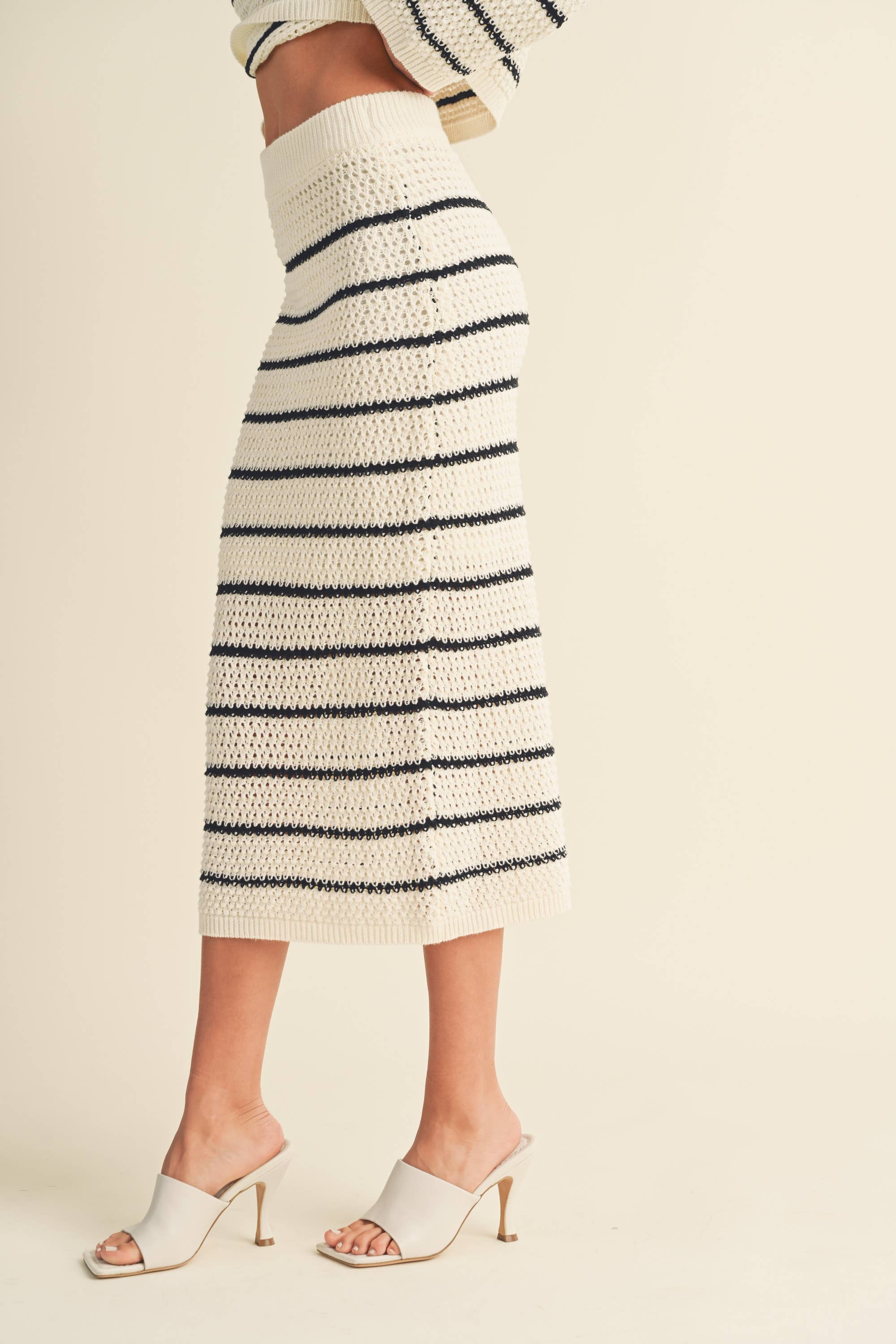 Woman wearing a high-waisted, ivory and black striped knit midi skirt with slide sandals.