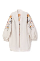Back view of a cream-colored kimono jacket with colorful floral embroidery, worn with matching light trousers.