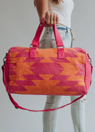 Bright orange and magenta woven weekender bag with geometric pattern, held by a woman in jeans
