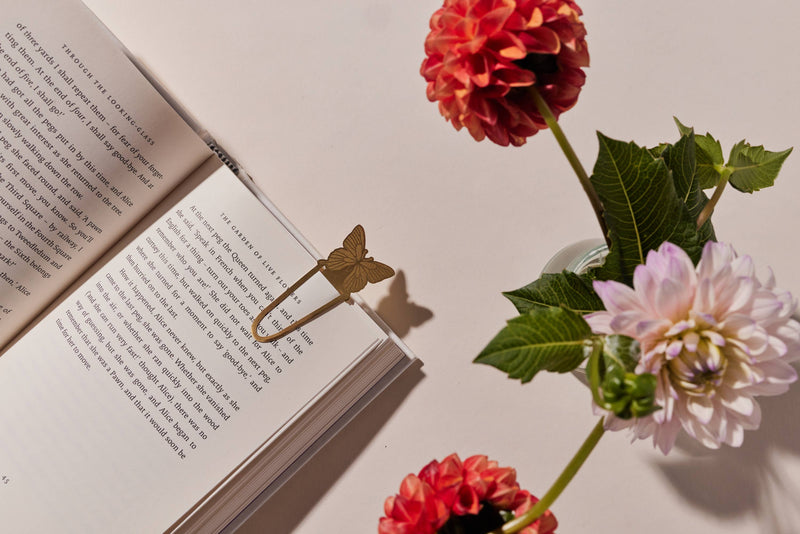 A set of two brass metal page tabs in butterfly and mushroom shapes, packaged on a pastel pink and white wavy background.