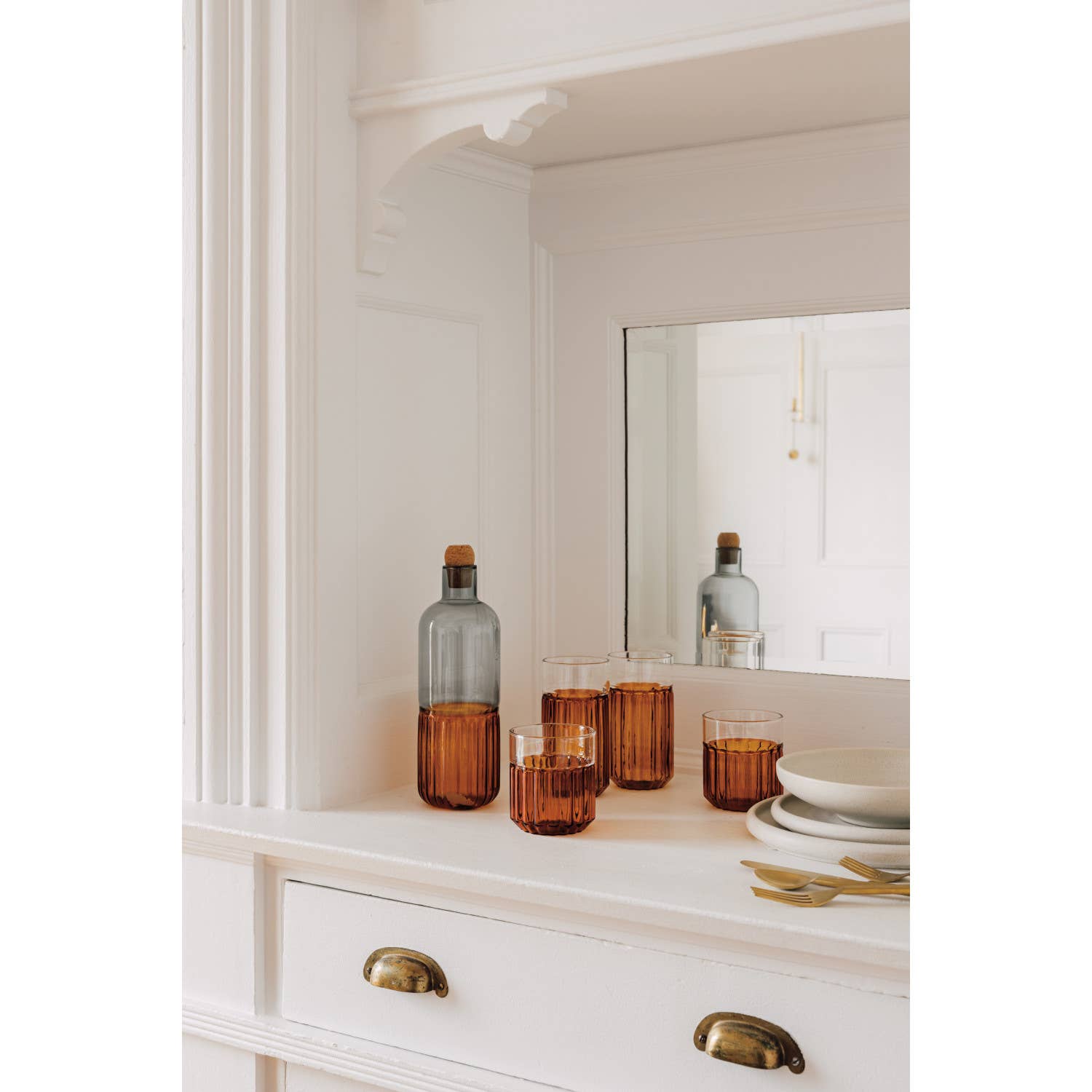 Decorative bottles and glasses on a white dresser with a mirror in the background.