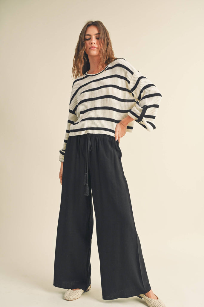 Woman wearing black wide-leg pants with smocked waistband and tassel drawstring.