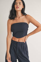 Woman wearing a strapless navy pinstriped crop top with tailored pleated pants.