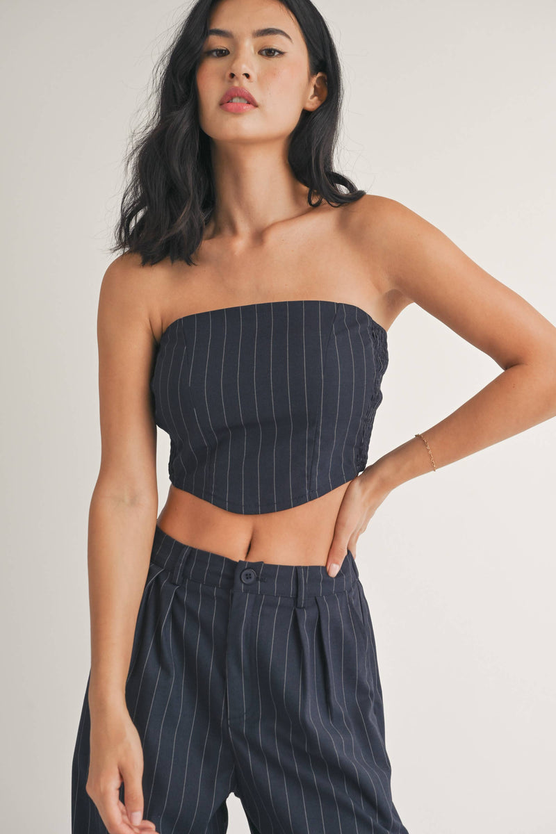 Woman wearing a strapless navy pinstriped crop top with tailored pleated pants.