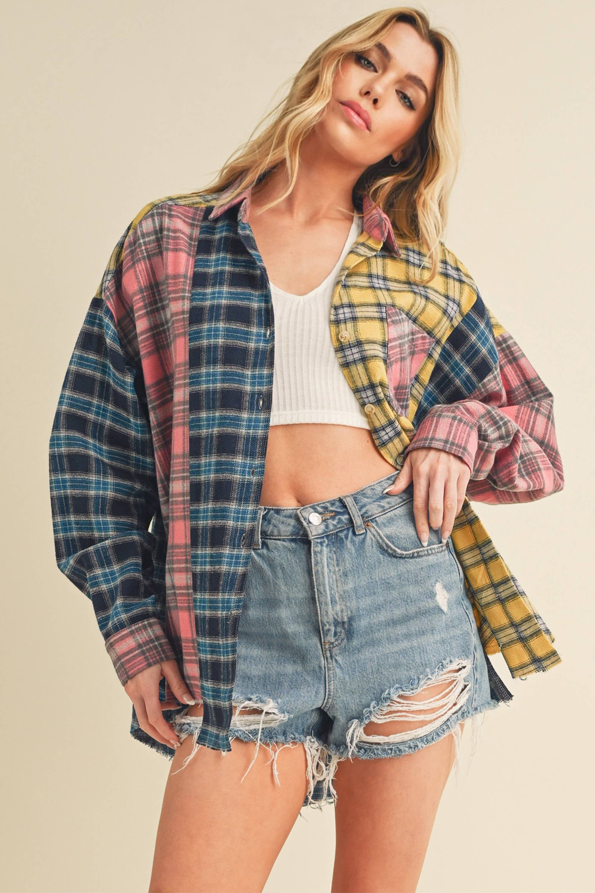 Woman wearing an oversized plaid colorblock flannel shirt in pink, yellow, and navy tones with raw hems.