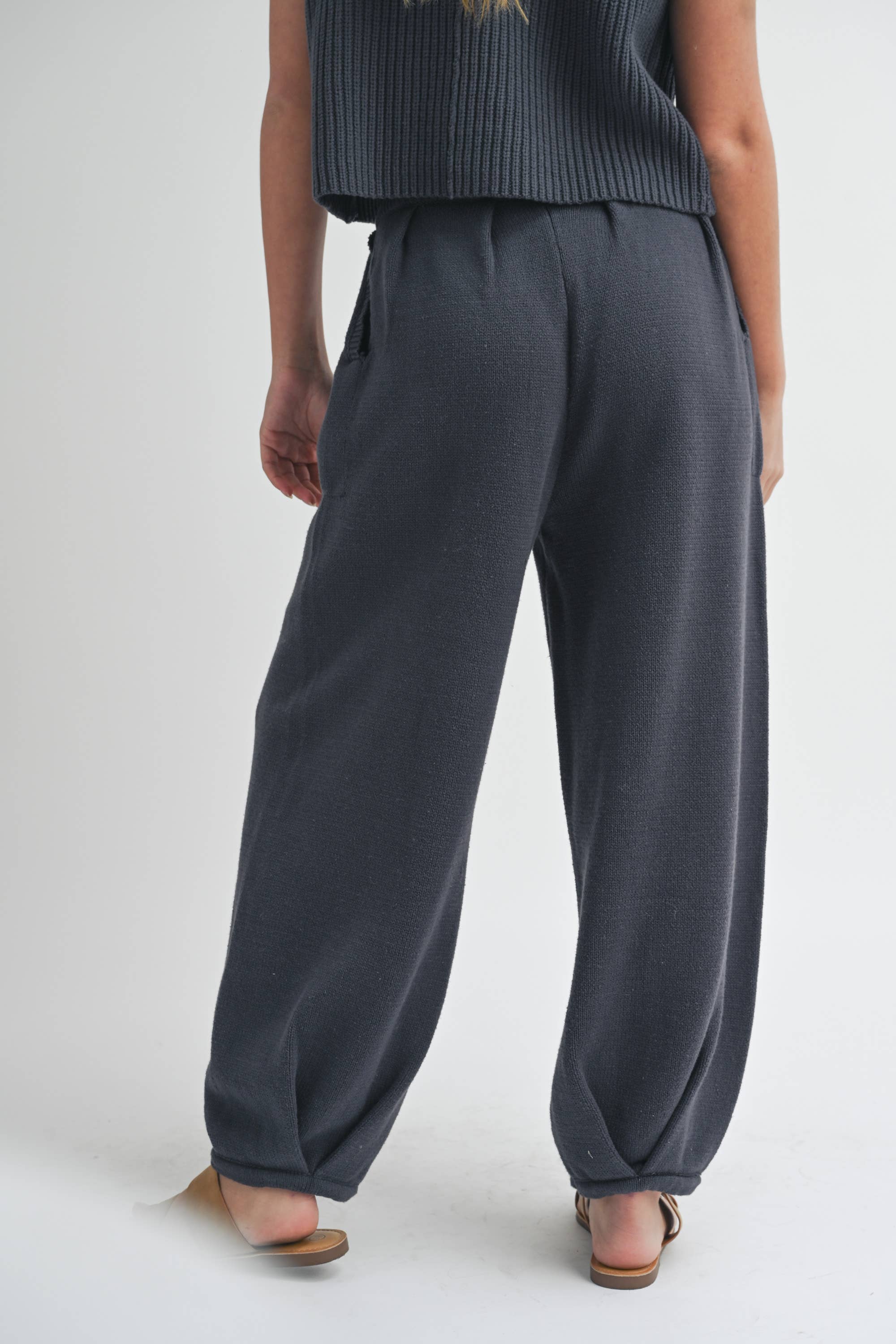 Woman wearing pleated bottom knitted pants in relaxed fit with drawstring waist and ankle detail.