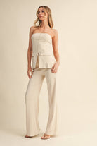 Woman wearing a beige strapless top and wide-leg pants on a beige background