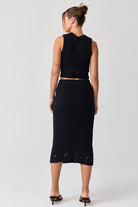 Woman wearing a black sleeveless crochet top and midi skirt set.