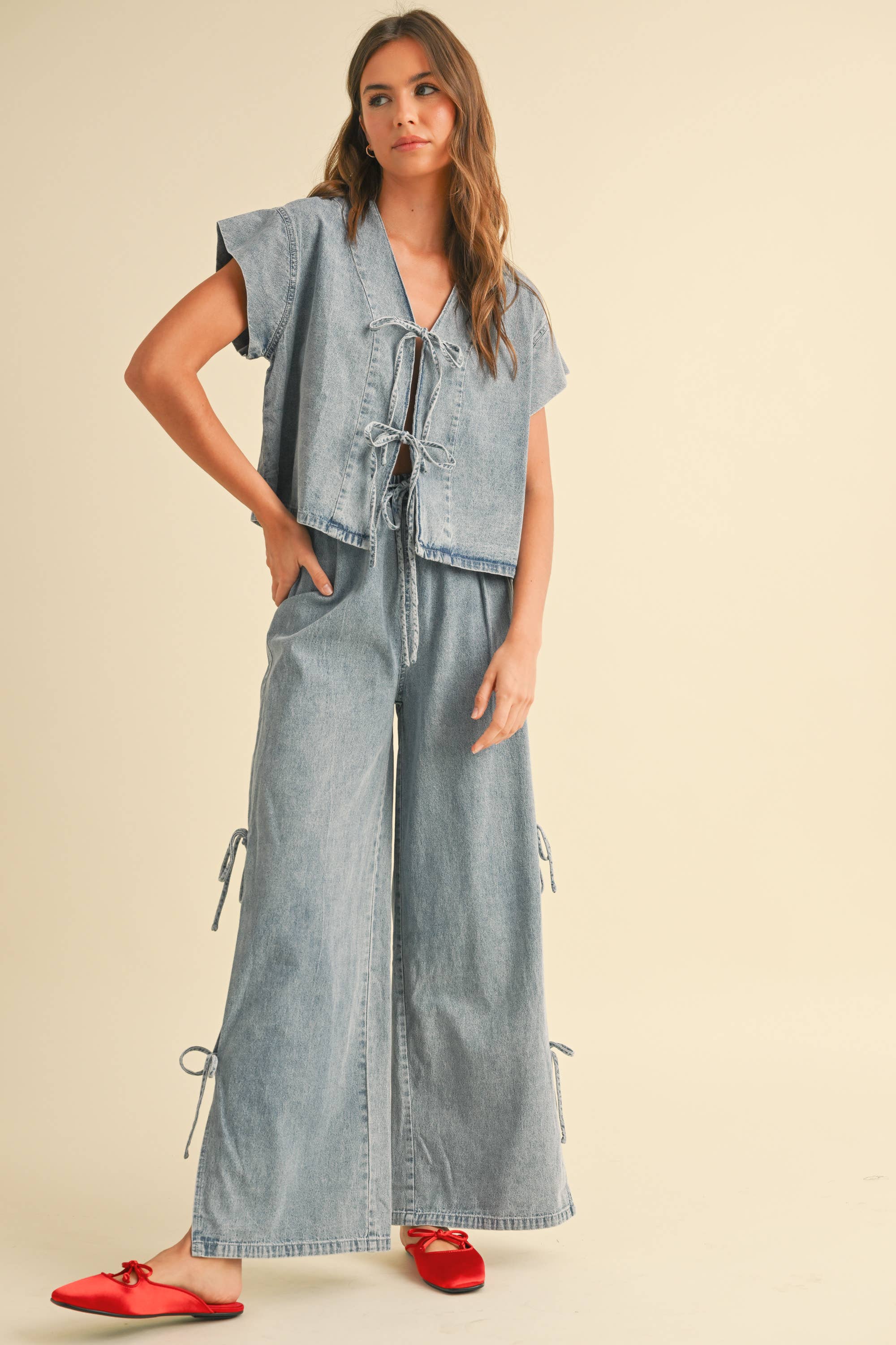 Woman wearing a light-wash denim two-piece set with tie-front top and wide-leg pants featuring side tie accents.