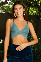 Model wearing a scalloped-edge lace bralette in burgundy and blue tones, styled with layered necklaces and velvet pants.