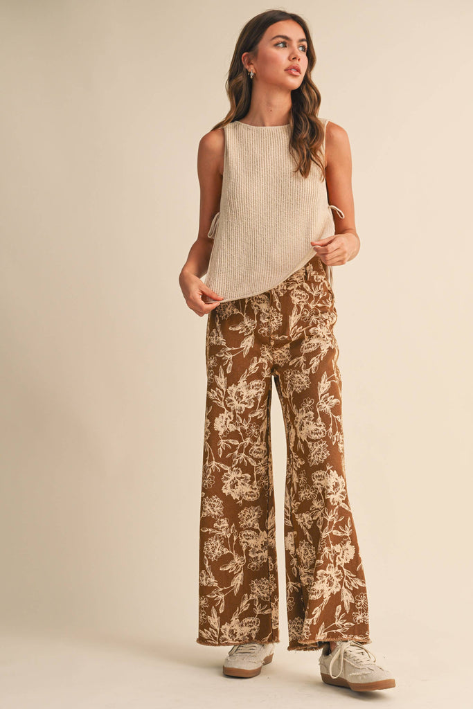 Woman wearing a beige ribbed knit tank top with side ties, paired with floral wide-leg pants