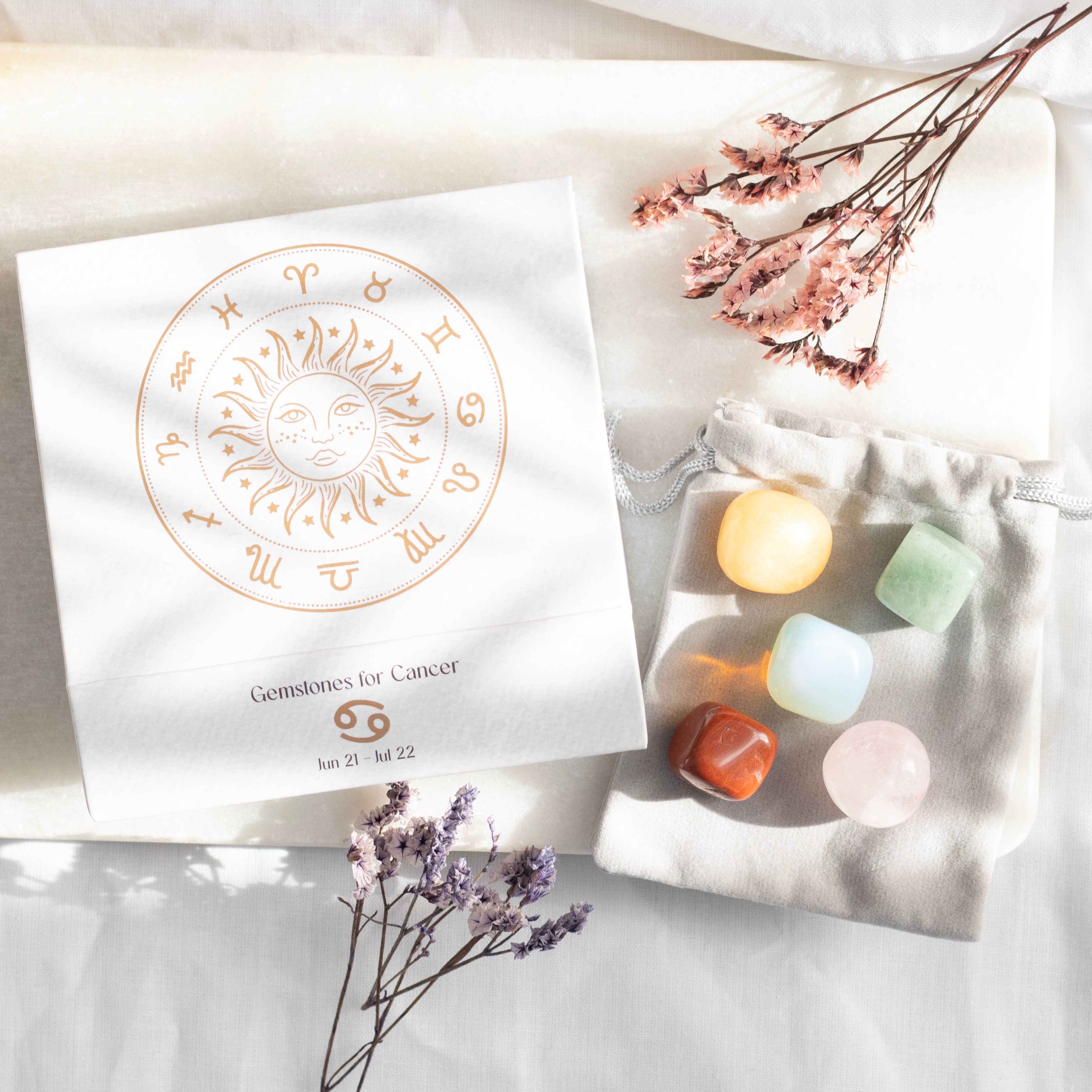 A Cancer zodiac gemstone set with five polished stones, including Moonstone, Rose Quartz, Red Jasper, Yellow Jade, and Green Aventurine, displayed in a decorative box with descriptions.