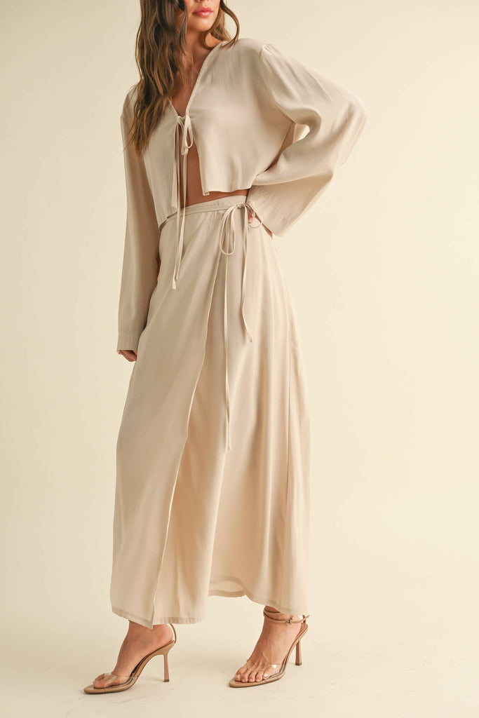 Woman wearing a beige tie-front long sleeve top and matching wrap maxi skirt, styled as a coordinated skirt set.