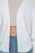 Woman wearing a white open-front cardigan with ribbed trim.