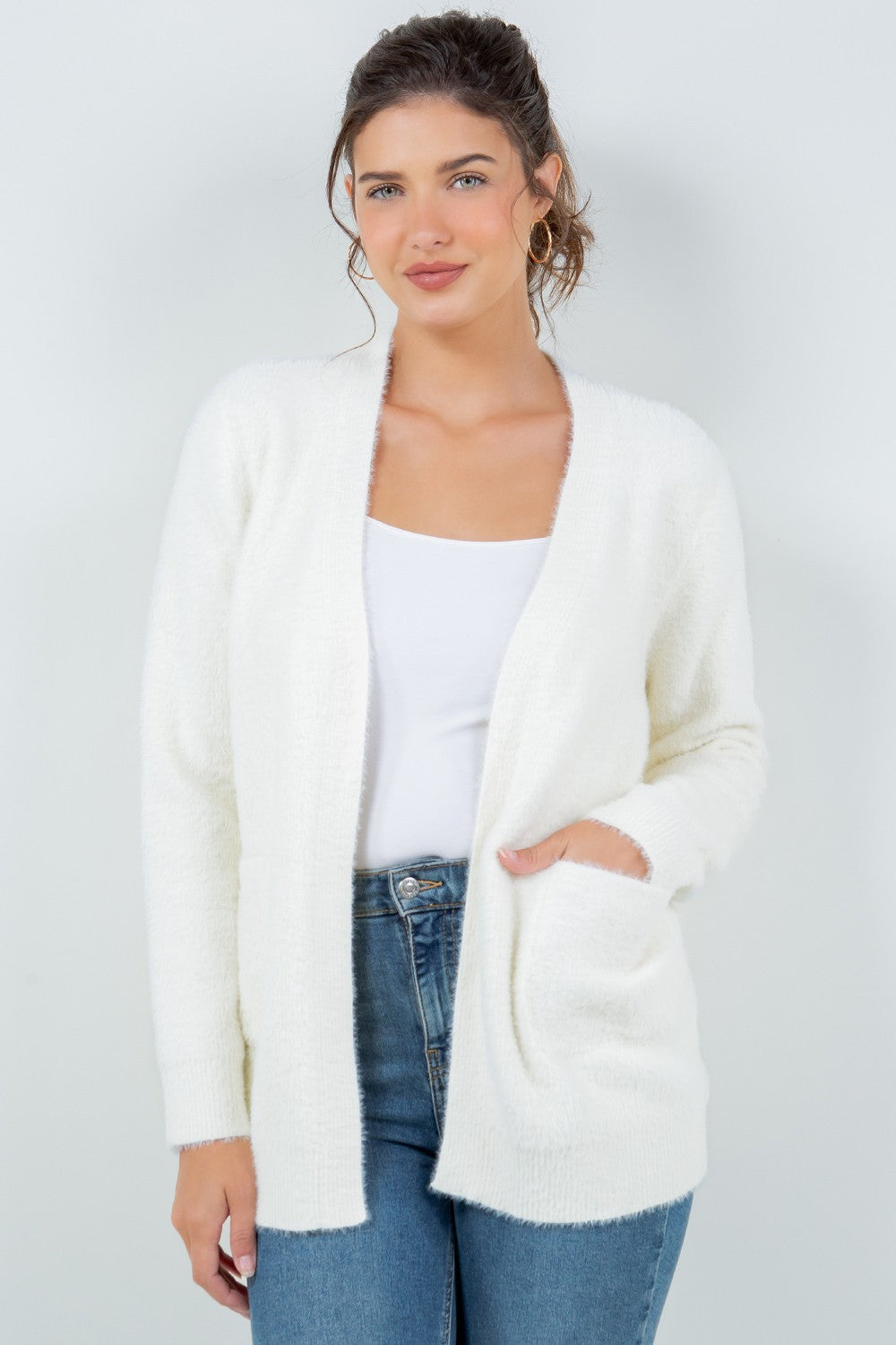 Woman wearing a soft white open-front cardigan with pockets.