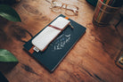 A white vegan leather notebook pouch with an embossed floral design, tan accents, and a gold zipper, attached to its packaging.