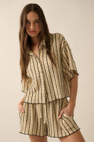 Woman wearing a beige striped two-piece lounge set with button-up shirt and matching drawstring shorts.
