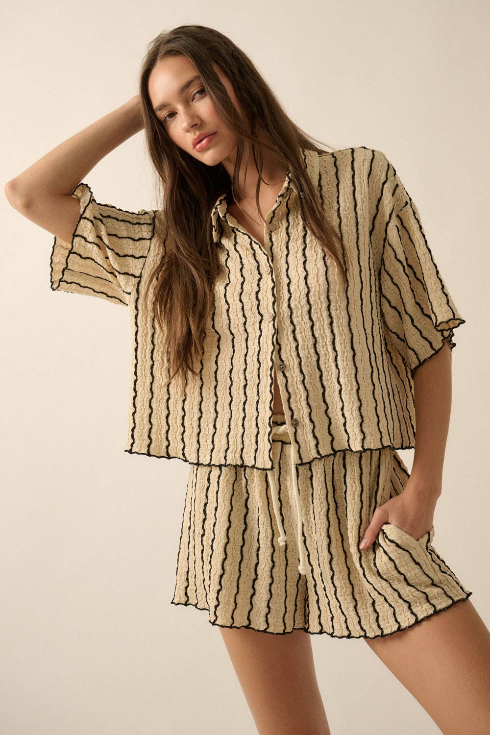 Woman wearing a beige striped two-piece lounge set with button-up shirt and matching drawstring shorts.