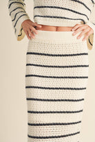 Woman wearing a high-waisted, ivory and black striped knit midi skirt with slide sandals.