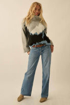 Person wearing a patterned sweater and jeans on a plain background