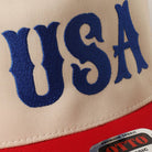 Close-up of a cap with 'USA' embroidered in blue on a beige background.