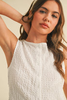 Model wearing a white sleeveless textured two-piece set featuring a cropped top and matching shorts with pockets.