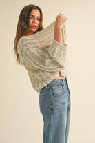 Woman wearing a loose cable knit cardigan with wide sleeves, paired with a white ribbed tank and blue denim jeans.