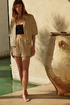Woman wearing a beige striped two-piece lounge set with button-up shirt and matching drawstring shorts.