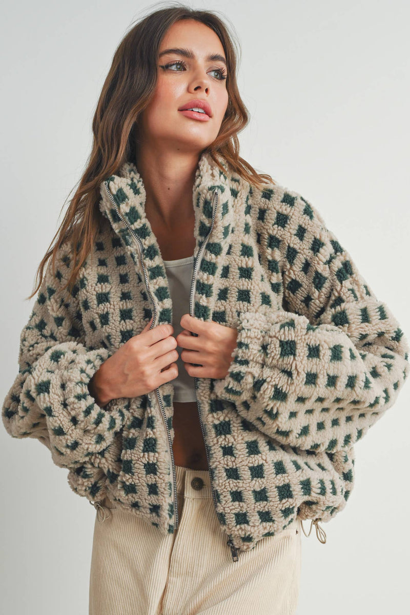 Woman wearing a beige and green checkered fleece jacket with a zip closure, paired with a white crop top and beige corduroy pants.