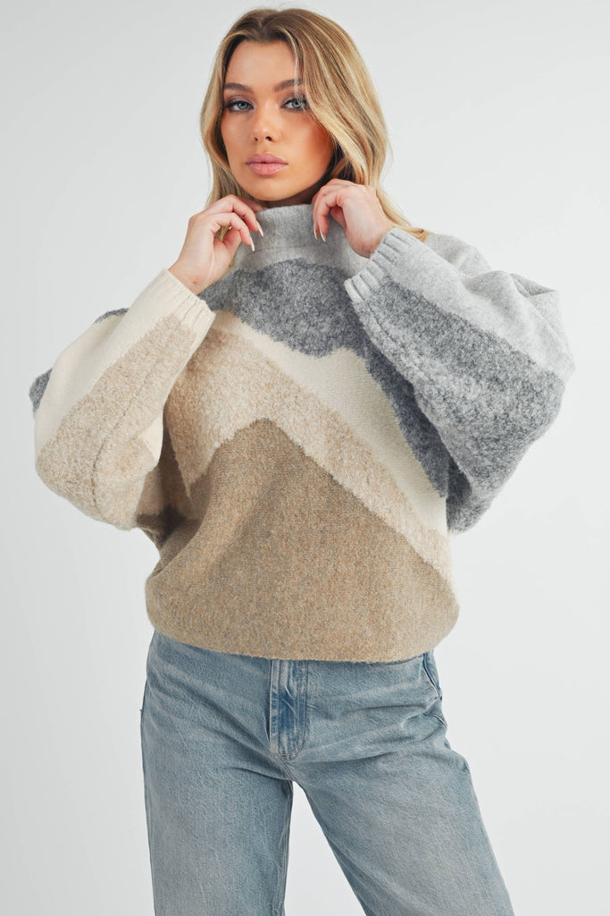 Front and back view of a woman wearing a color-block knit sweater in grey, cream, and taupe with a relaxed fit.