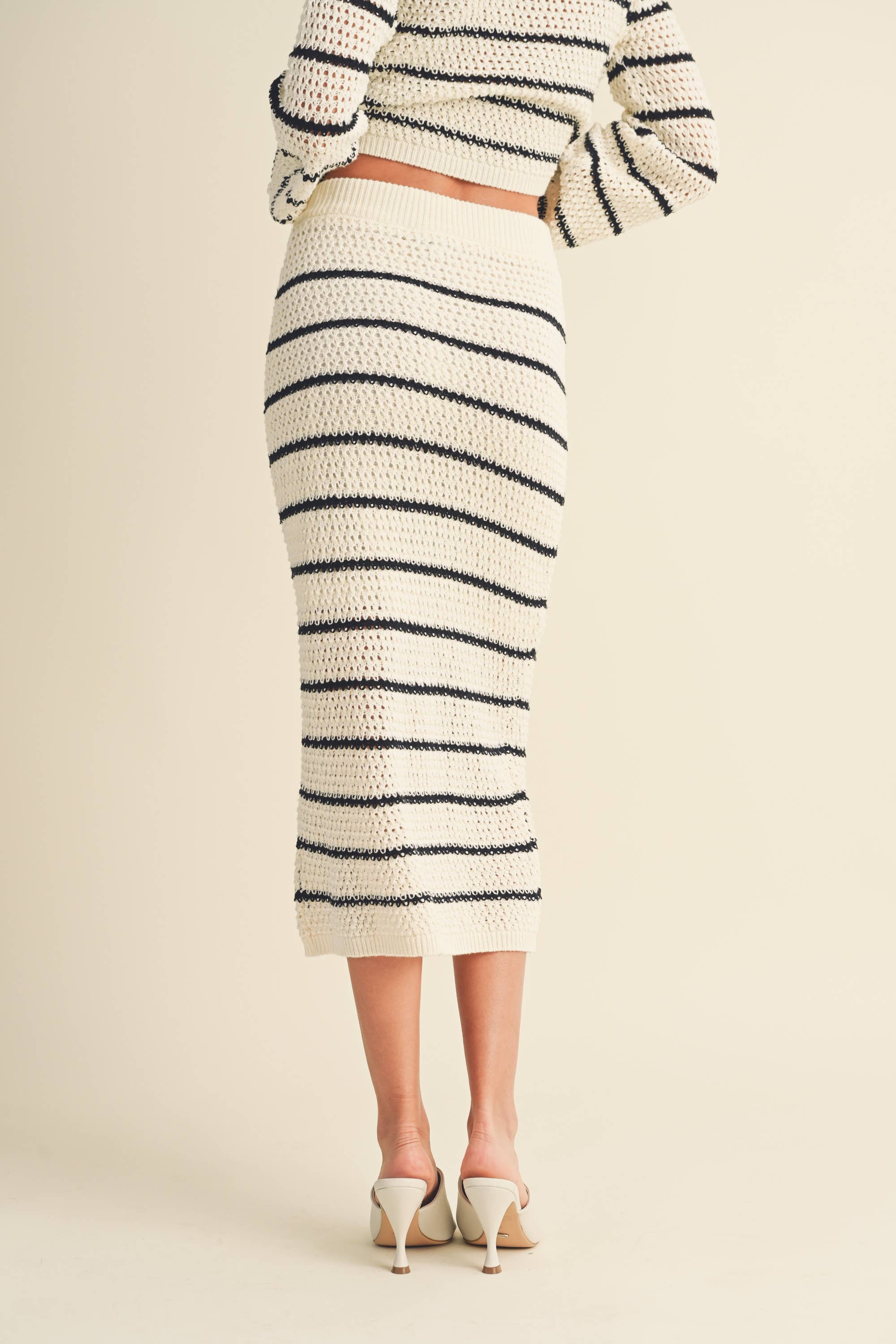 Woman wearing a high-waisted, ivory and black striped knit midi skirt with slide sandals.