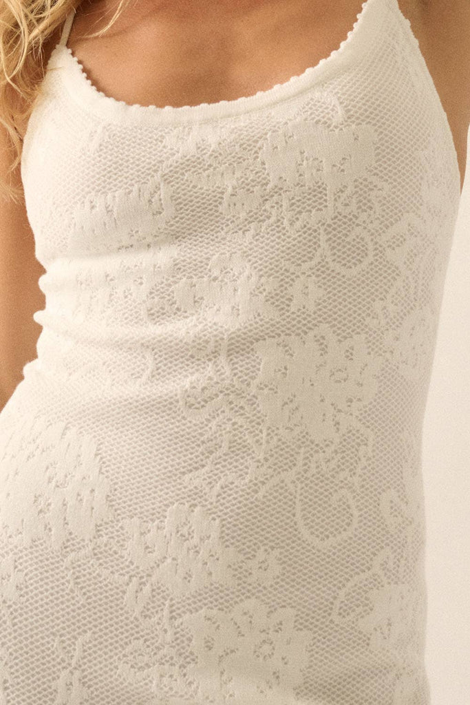 Woman wearing a sheer white lace maxi dress with spaghetti straps and floral detailing.