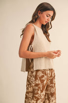 Woman wearing a beige sleeveless top and brown floral pants against a plain background