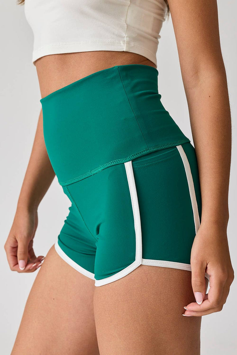 Woman wearing high-waist red shorts with white contrast piping. / Woman wearing high-waist green shorts with white contrast piping.